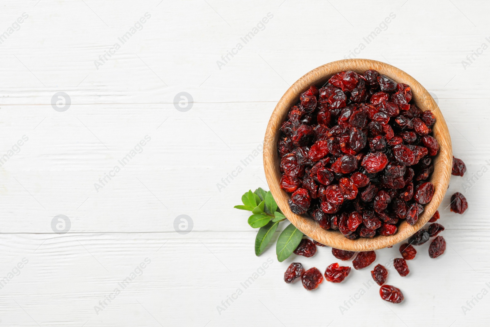 Photo of Tasty dried cranberries and leaves on white table, flat lay. Space for text