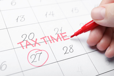 Image of Woman writing words TAX TIME on calendar, closeup