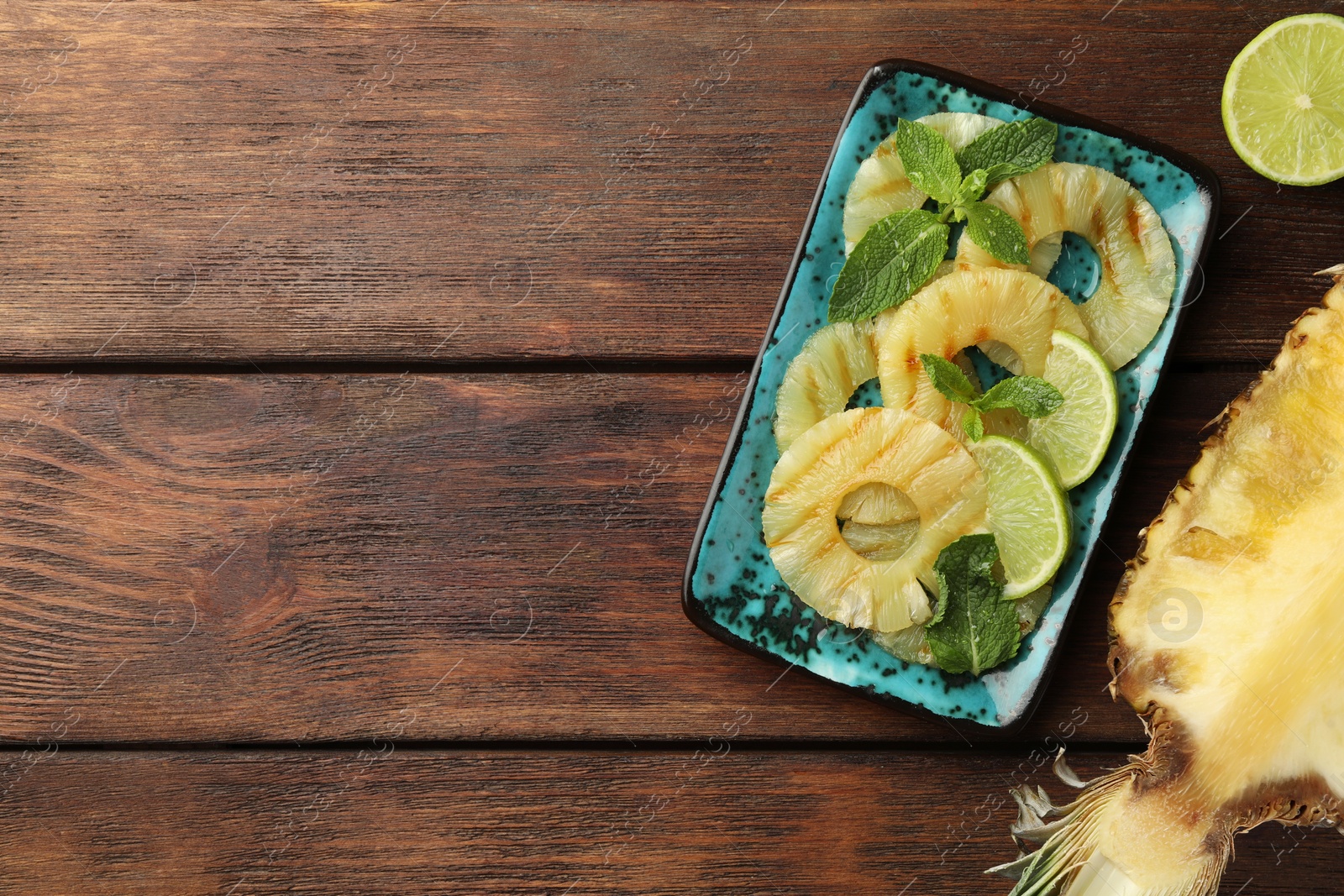 Photo of Tasty grilled pineapple slices, mint and cut lime on wooden table, flat lay. Space for text