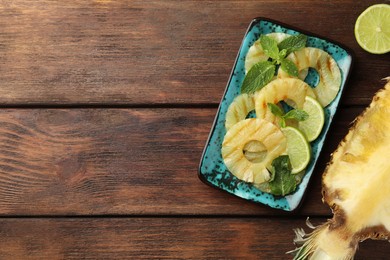 Photo of Tasty grilled pineapple slices, mint and cut lime on wooden table, flat lay. Space for text