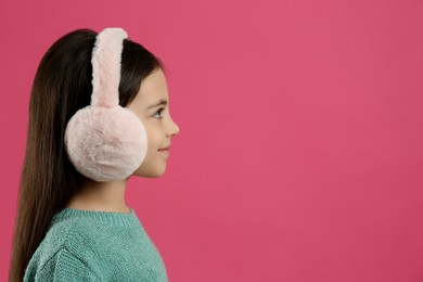 Photo of Cute little girl wearing stylish earmuffs on pink background. Space for text