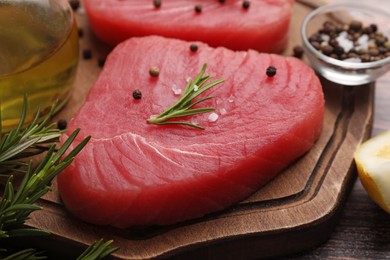 Photo of Raw tuna fillet with rosemary and peppercorns on wooden board, closeup