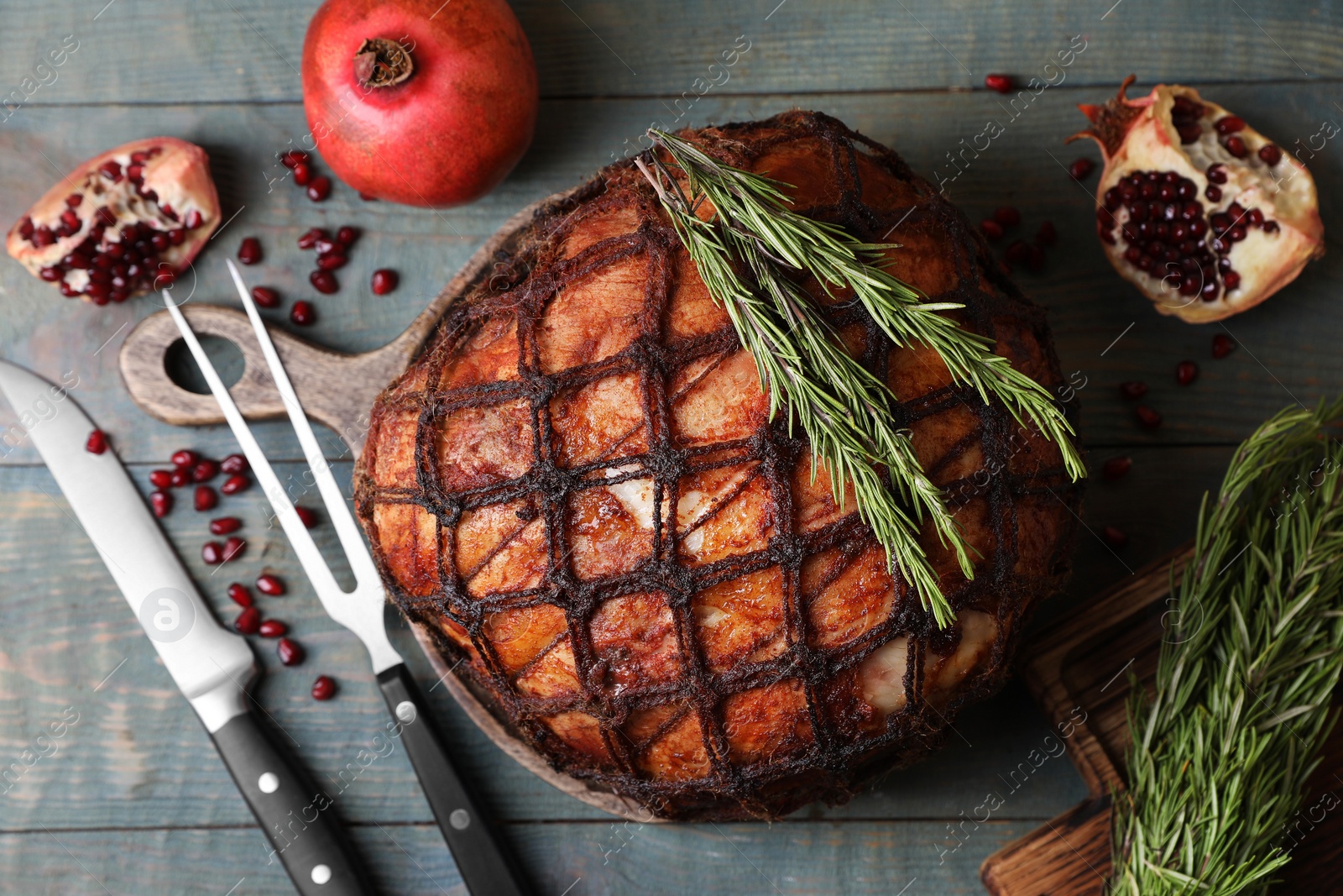 Photo of Delicious baked ham, knife, carving fork, pomegranate and rosemary on rustic wooden table, flat lay