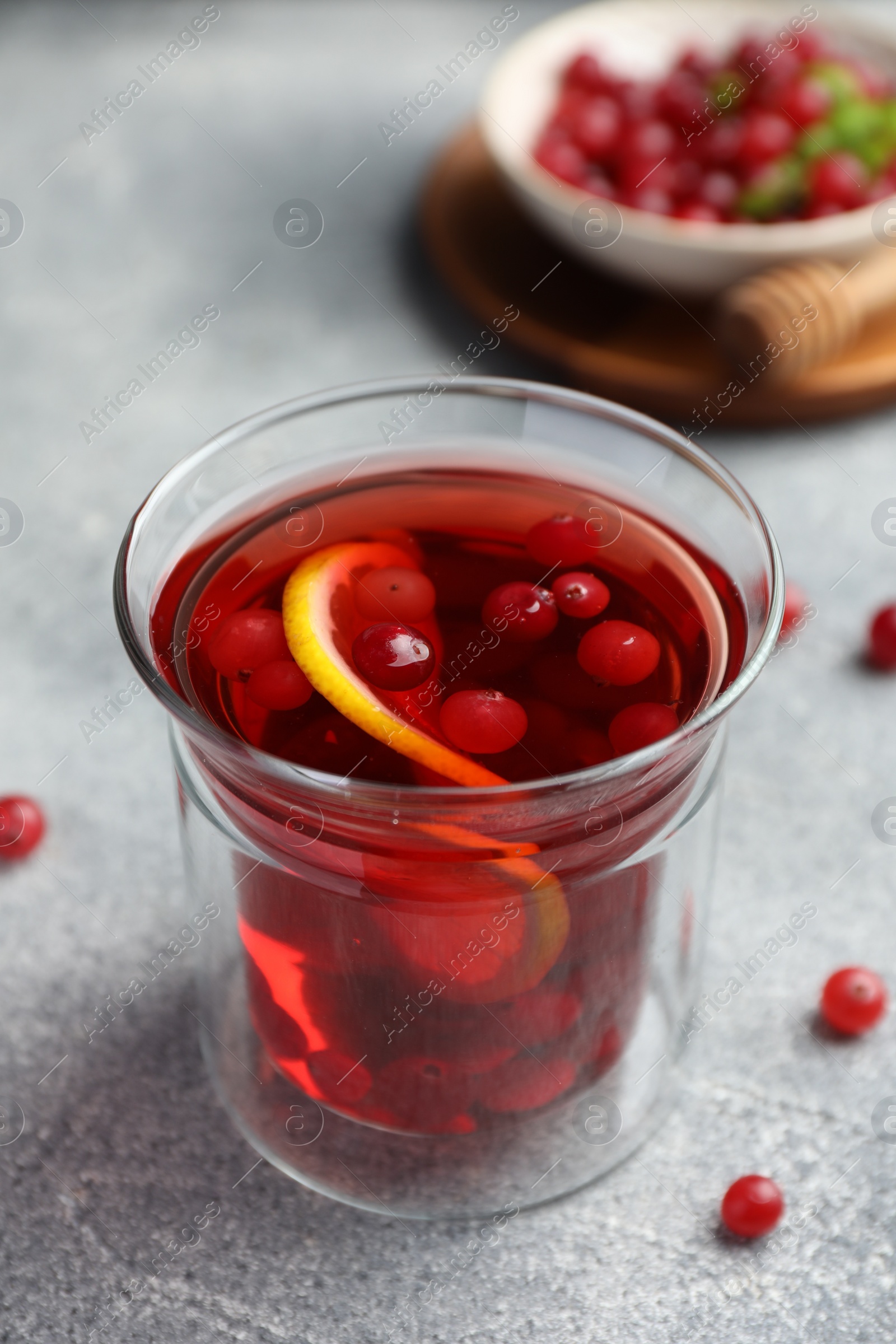 Photo of Tasty hot cranberry tea with lemon and fresh berries in glass on light grey textured table