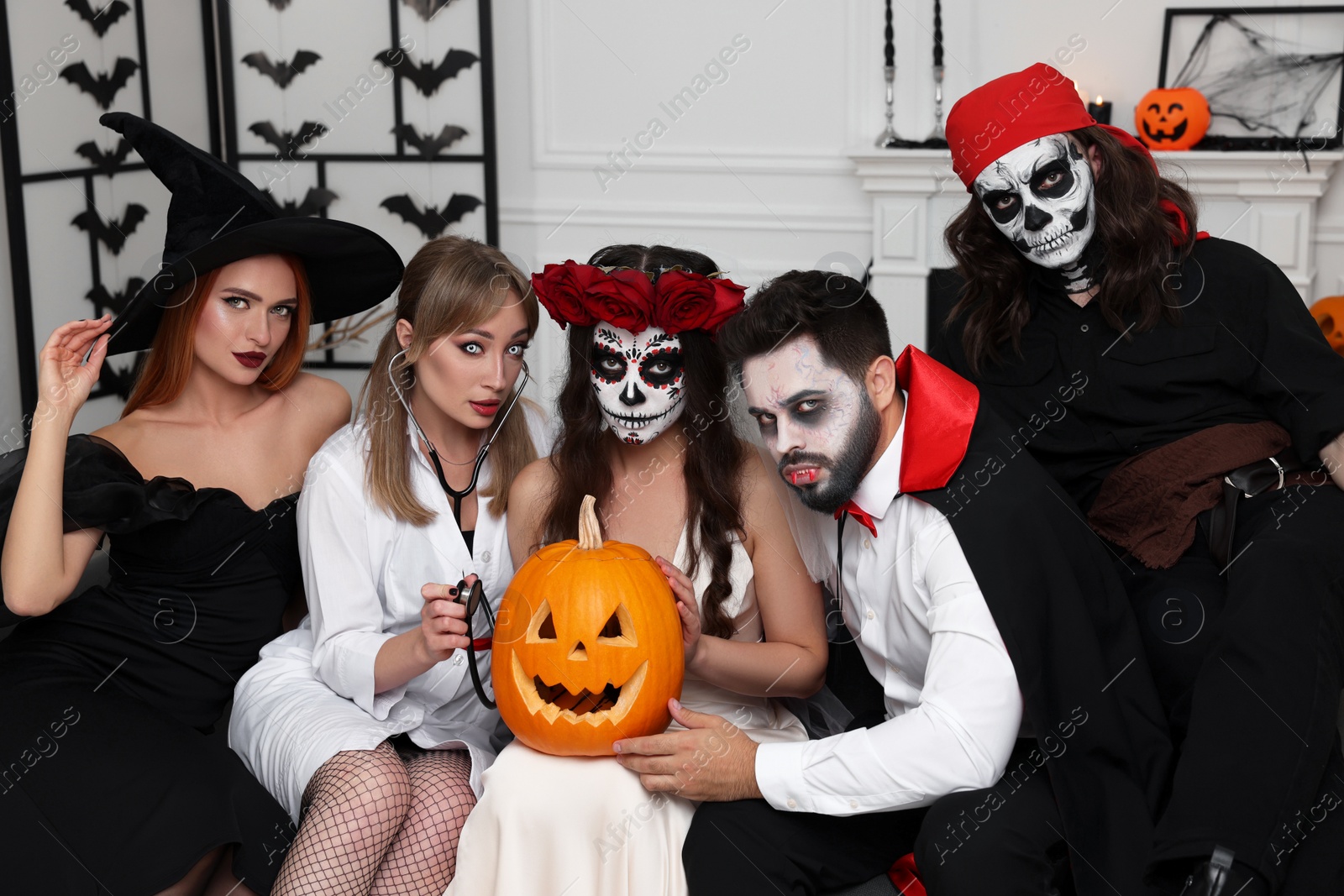 Photo of Group of people in scary costumes with carved pumpkin indoors. Halloween celebration