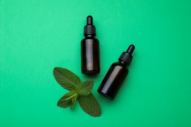 Photo of Bottles of essential oil and mint on green background, flat lay