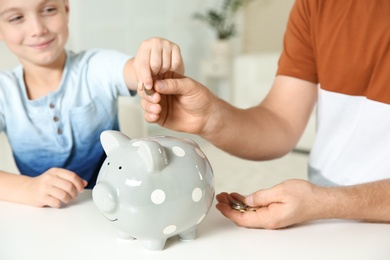 Father and son putting coin into piggy bank on blurred background, closeup