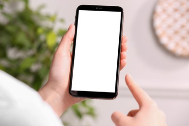 Woman holding smartphone with blank screen indoors, closeup. Mockup for design