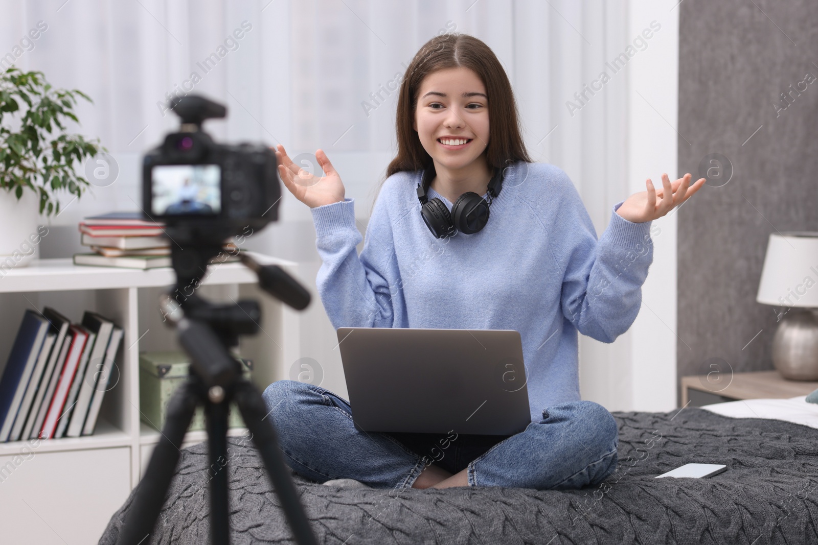 Photo of Smiling teenage blogger with laptop explaining something while streaming at home