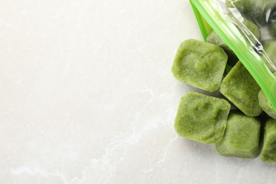 Frozen broccoli puree cubes in plastic bag on white marble table, top view. Space for text