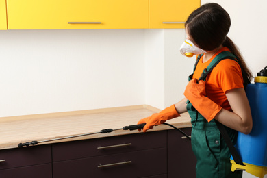 Pest control worker spraying pesticide in kitchen