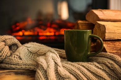 Photo of Green cup with hot drink and blanket on table against fireplace