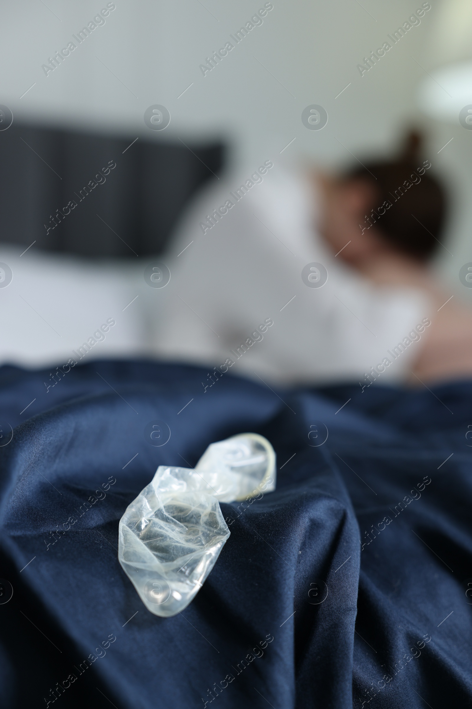 Photo of Woman sitting on bed and unrolled condom in bedroom, selective focus. Safe sex
