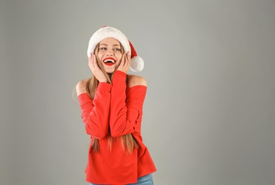 Photo of Young beautiful woman in Santa hat on grey background. Christmas celebration