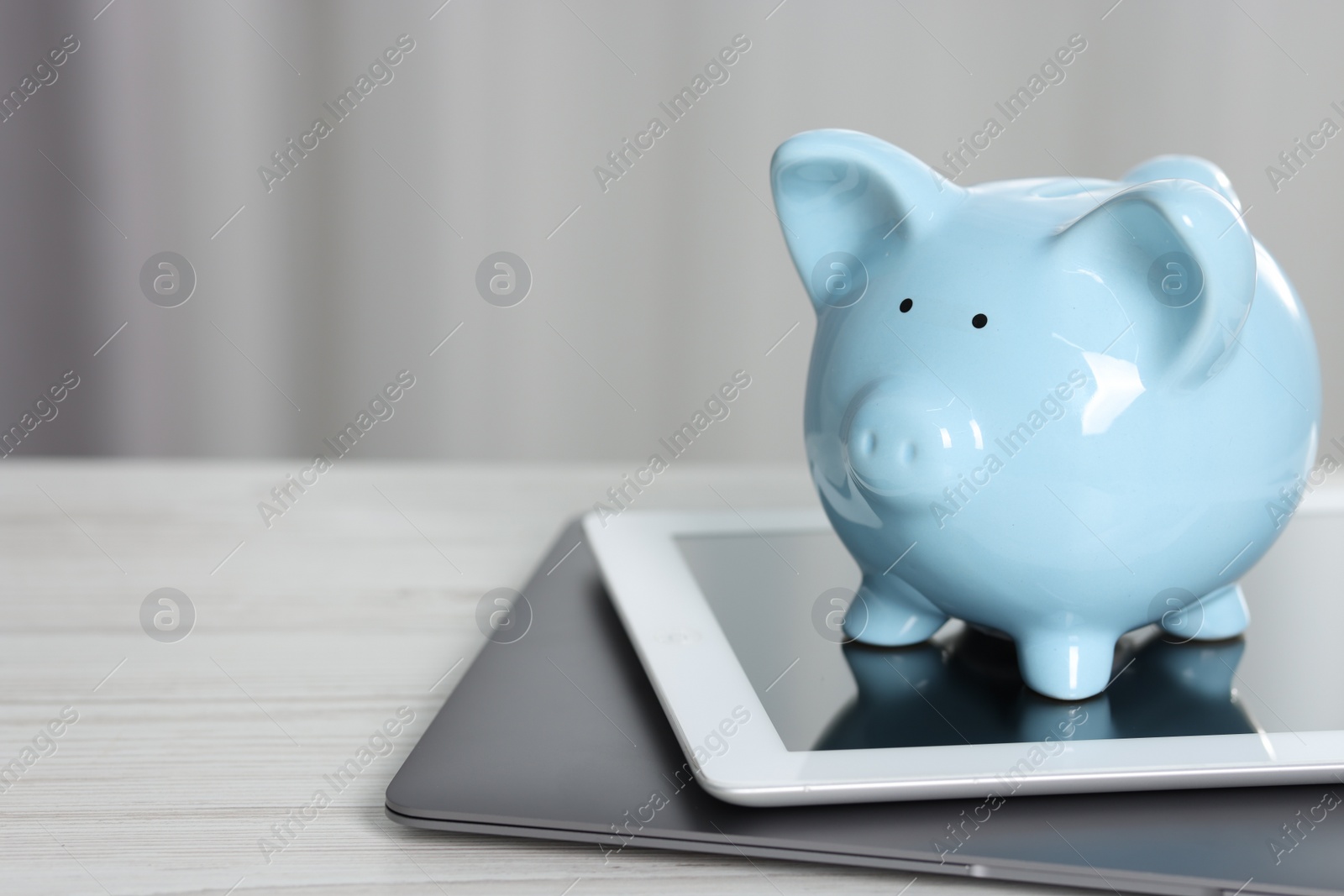 Photo of Piggy bank, tablet and laptop on white table indoors. Space for text