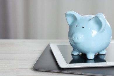 Photo of Piggy bank, tablet and laptop on white table indoors. Space for text