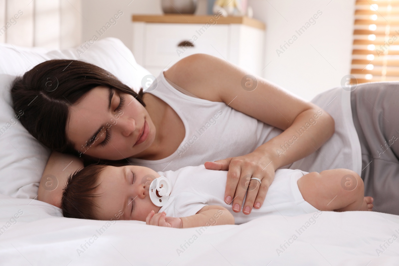 Photo of Young mother resting near her sleeping baby on bed at home