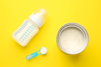 Feeding bottle with infant formula and powder on yellow background, flat lay