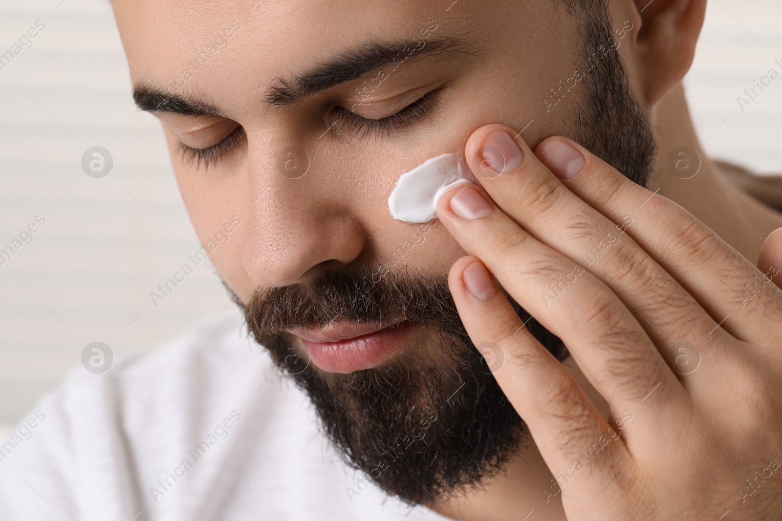 Photo of Man with dry skin applying cream onto his face on light background