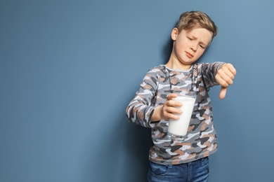Photo of Little boy with dairy allergy holding glass of milk on color background