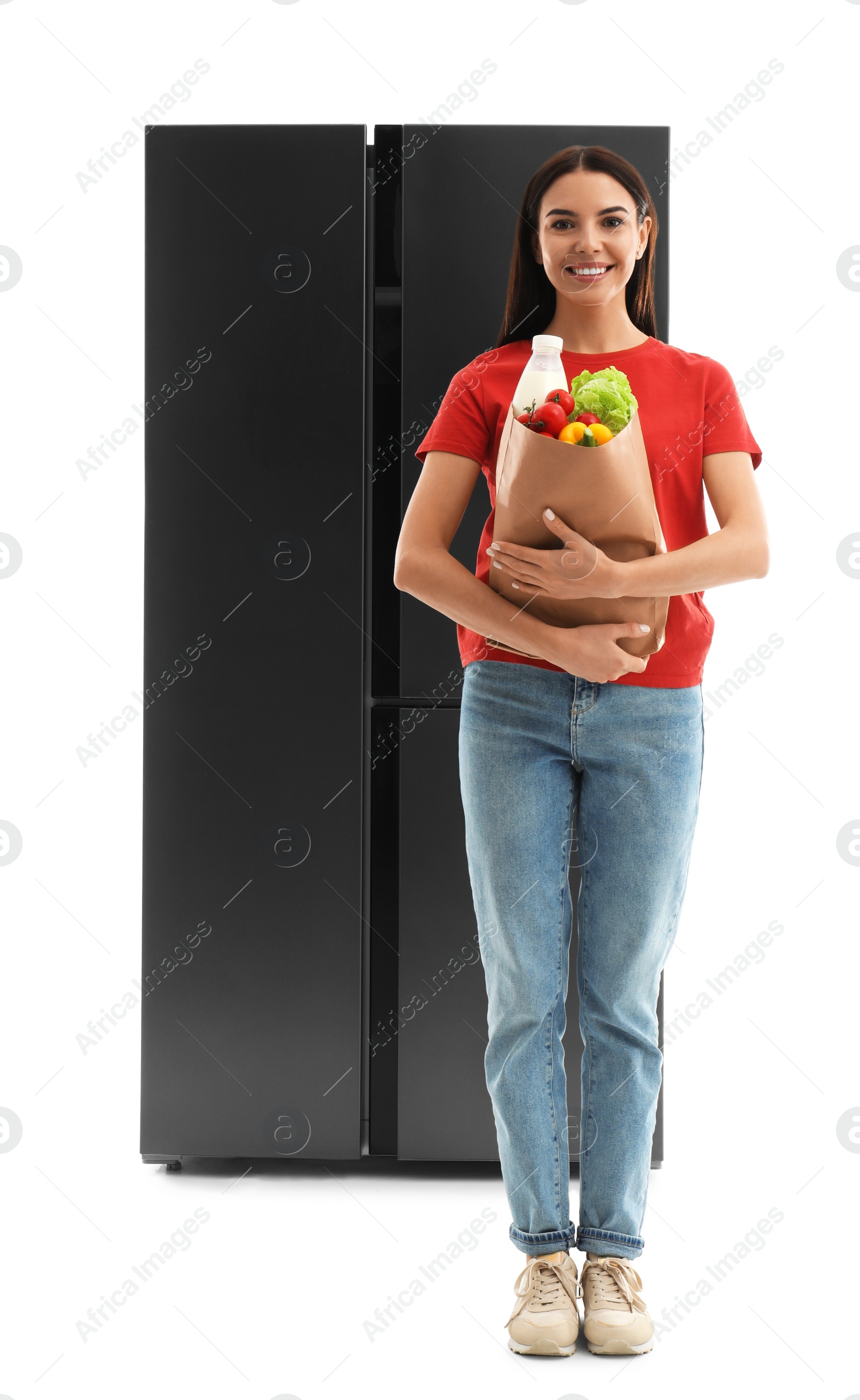 Photo of Young woman with bag of groceries near refrigerator on white background