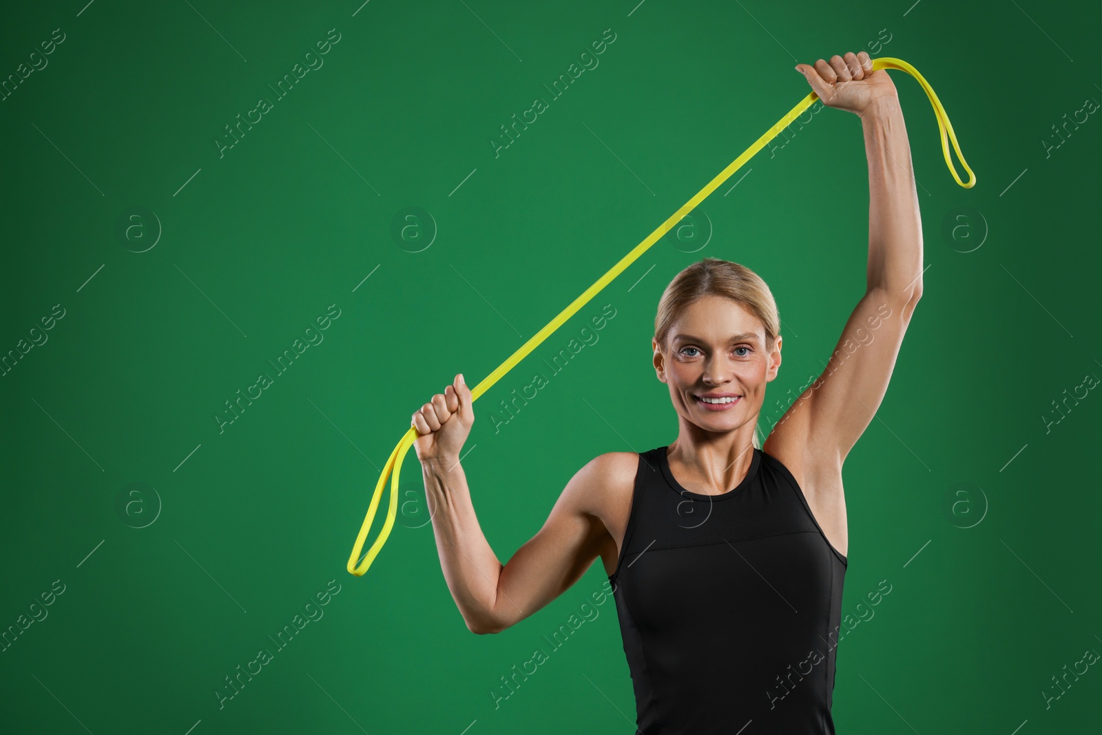 Photo of Smiling woman exercising with elastic resistance band on green background. Space for text