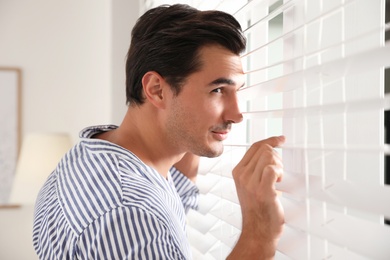 Portrait of handsome young man near window blinds indoors