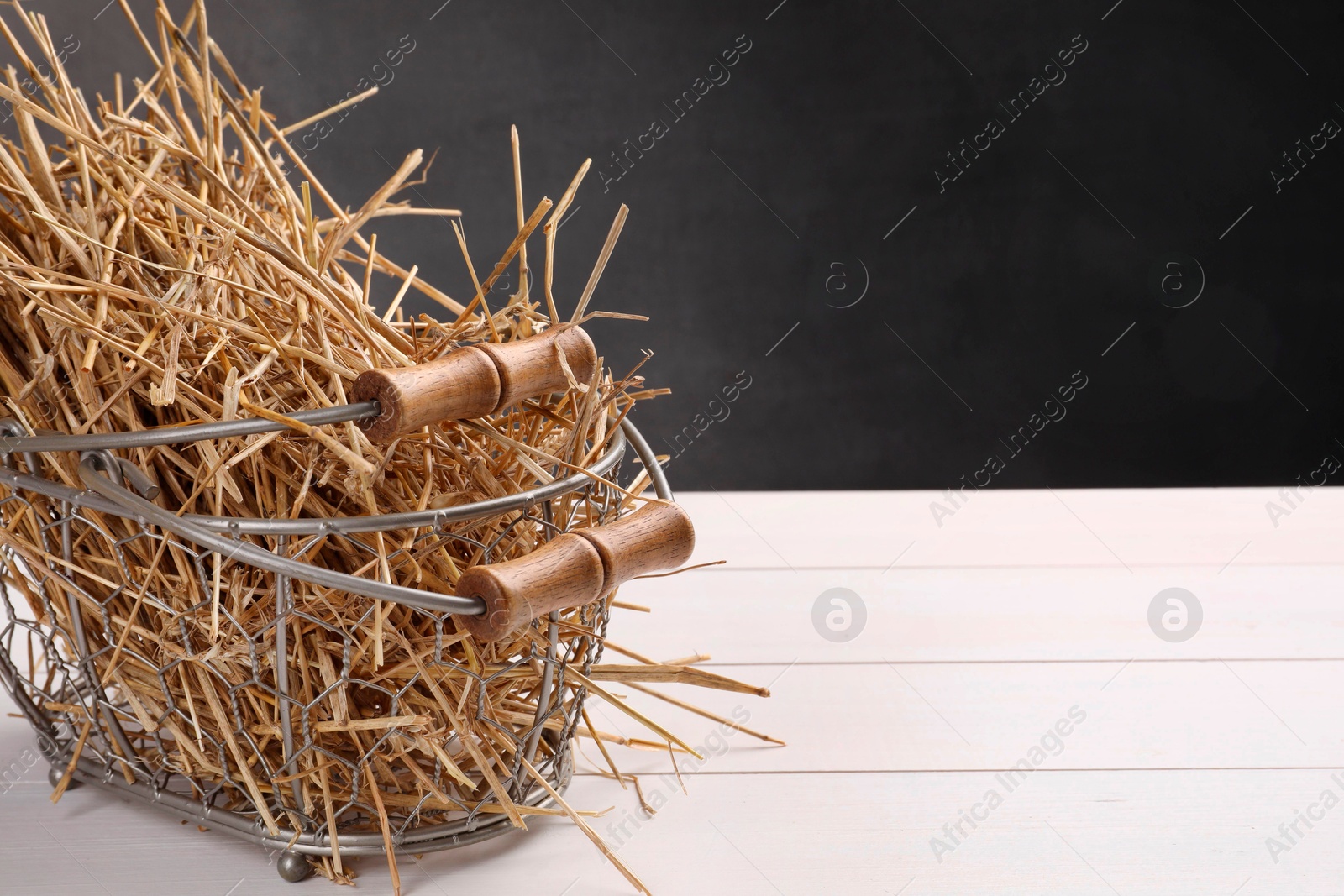 Photo of Dried straw in metal basket on white wooden table, space for text