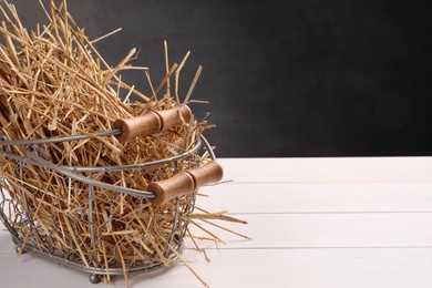 Dried straw in metal basket on white wooden table, space for text