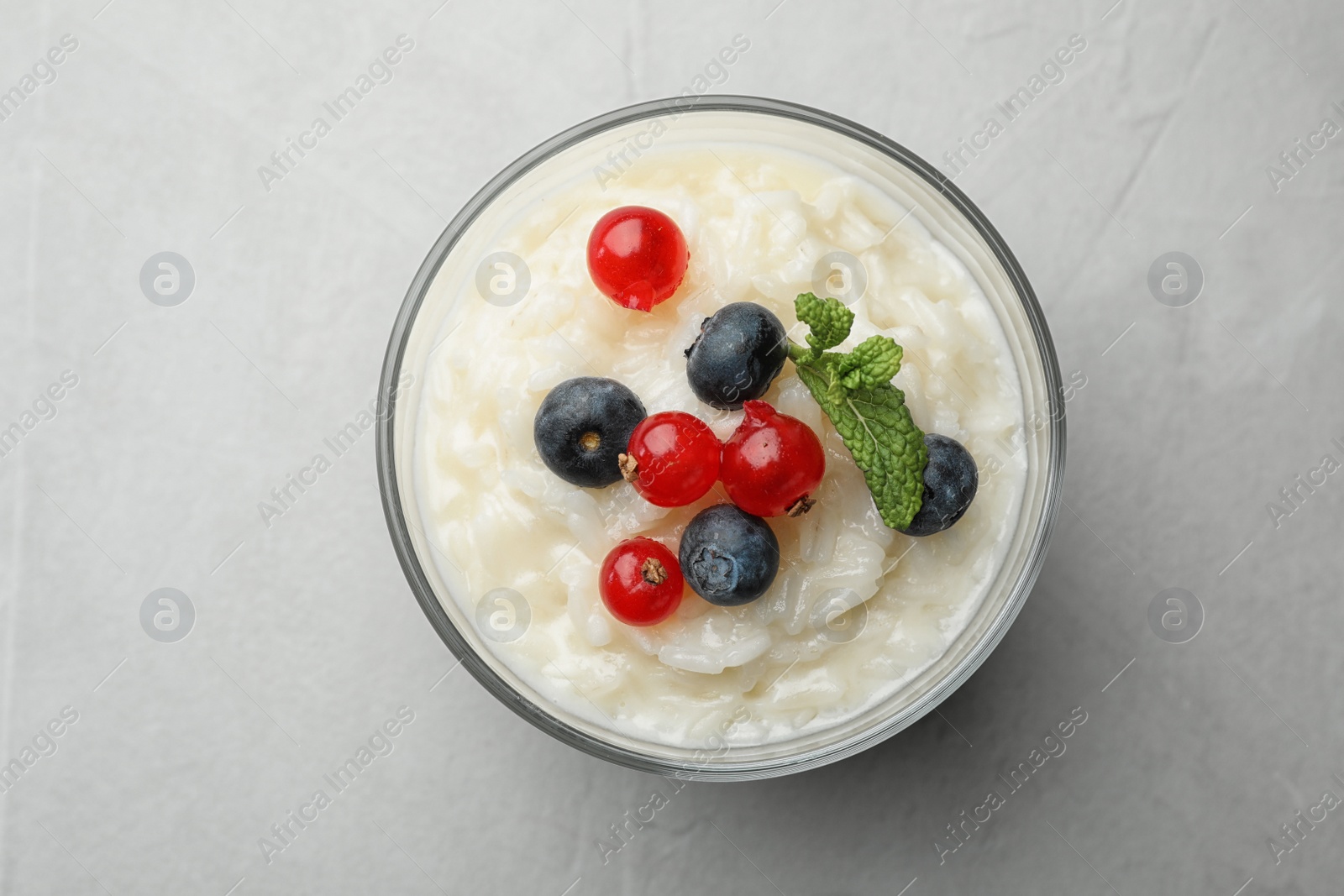 Photo of Delicious rice pudding with berries on light table, top view