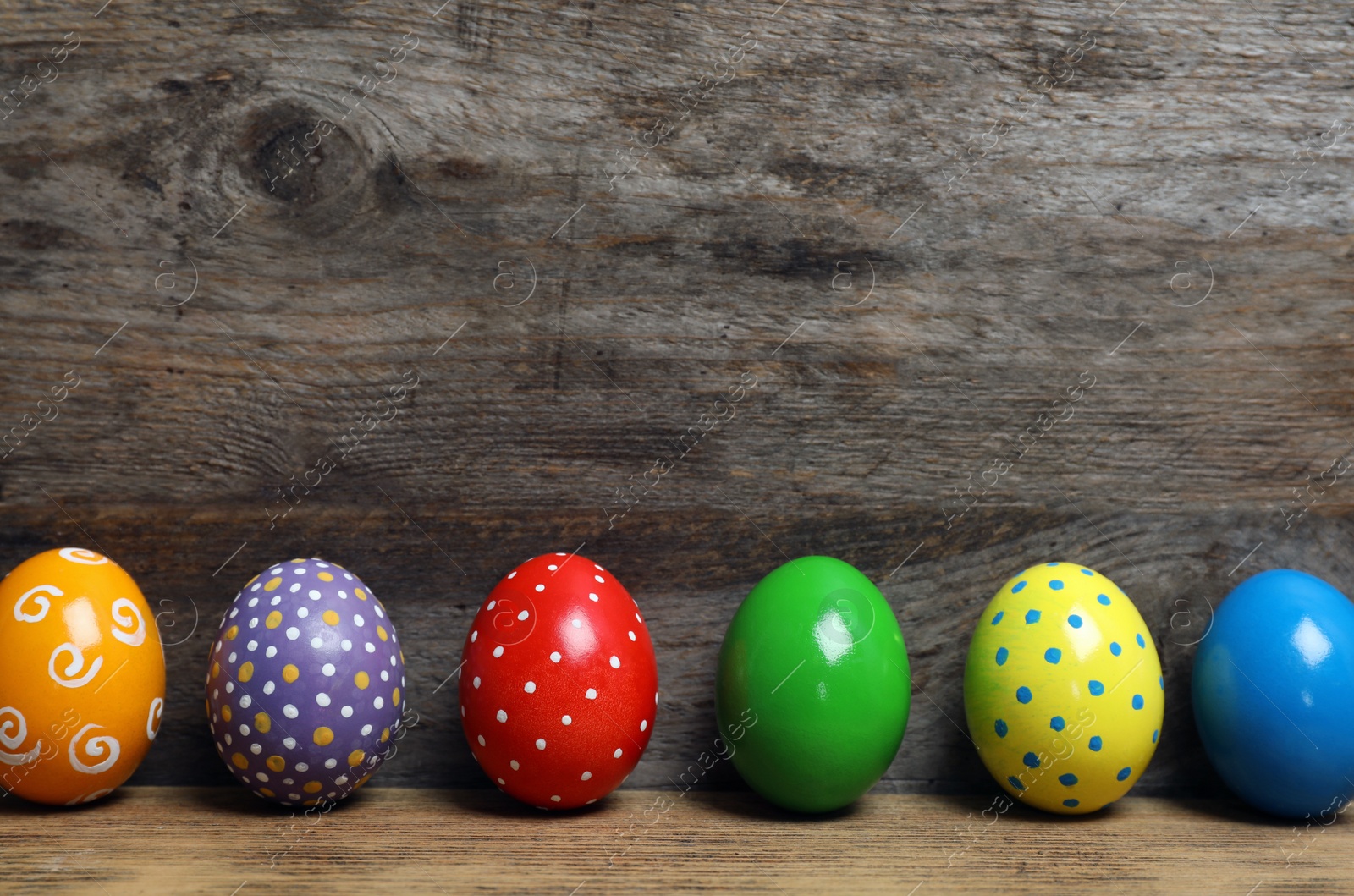 Photo of Decorated Easter eggs on table near wooden wall. Space for text