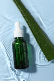 Photo of Bottle of cosmetic product and aloe leaf in water on light blue background, flat lay