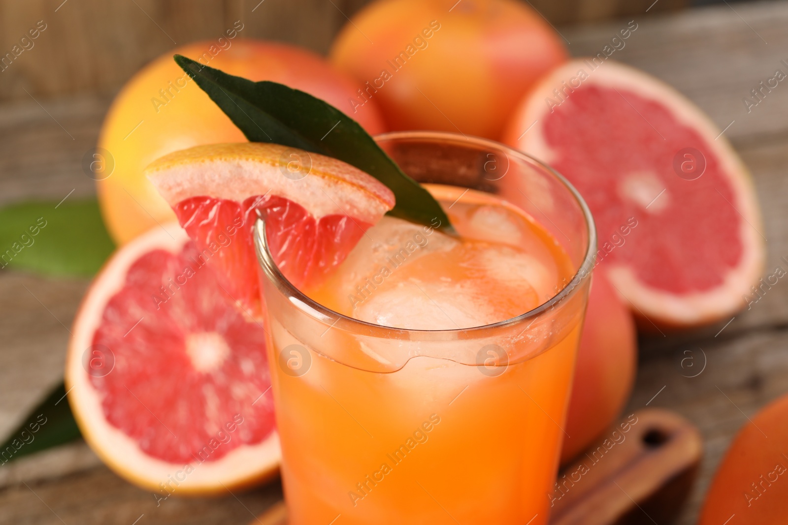 Photo of Tasty grapefruit drink with ice, slice of fruit and leaf in glass on table, closeup