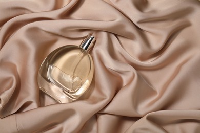 Luxury perfume in bottle on beige silk fabric, top view