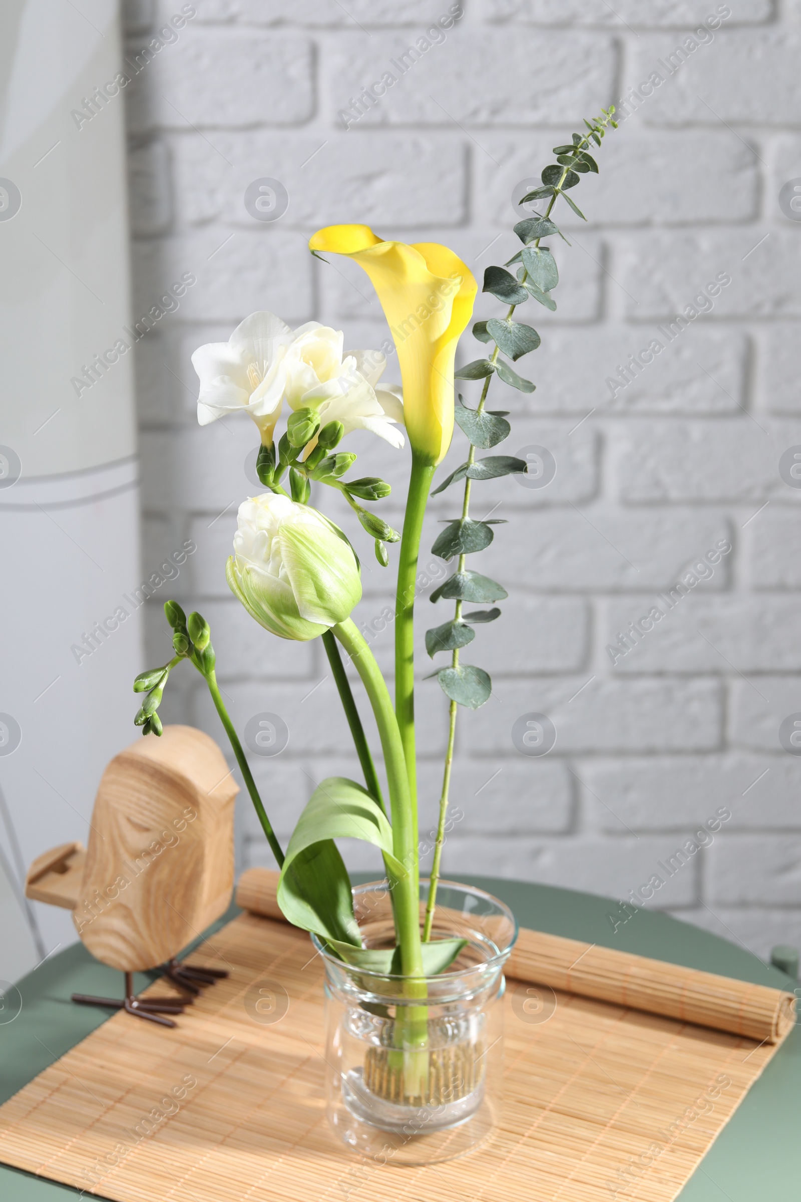 Photo of Beautiful ikebana for stylish house decor. Floral composition with fresh flowers and eucalyptus branch on coffee table near white brick wall