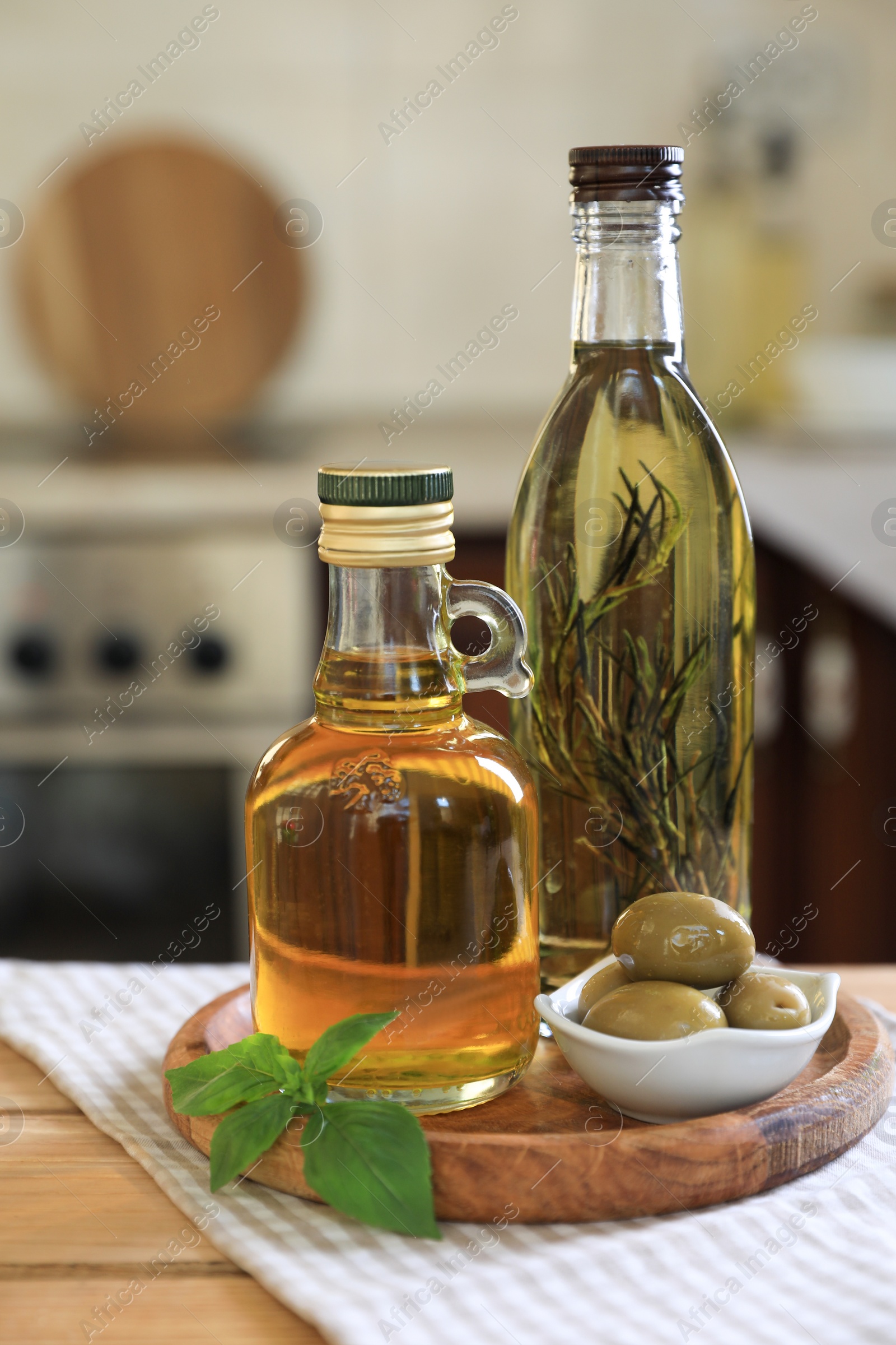 Photo of Different cooking oils, olives and basil on wooden table in kitchen