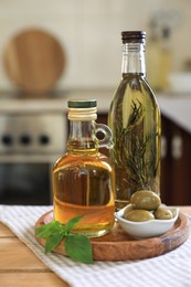 Photo of Different cooking oils, olives and basil on wooden table in kitchen