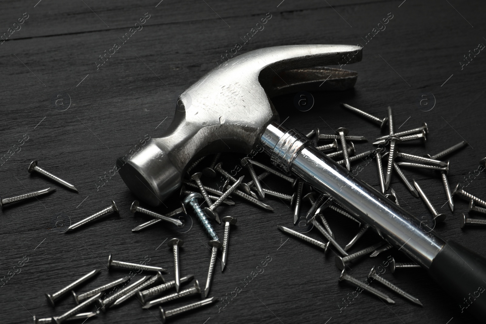 Photo of New hammer and metal nails on black wooden table, closeup. Professional construction tool