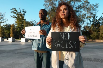 Photo of African American woman and man holding signs with phrase Say No To Racism outdoors