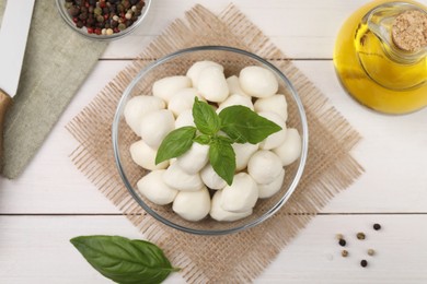 Flat lay composition with tasty mozzarella balls and basil leaves on white wooden table