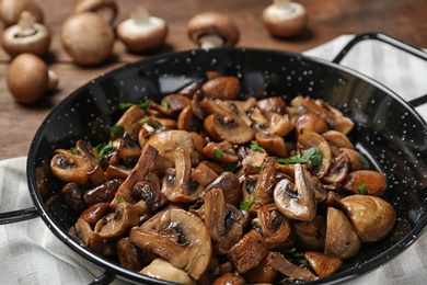 Photo of Frying pan with mushrooms on wooden table, closeup