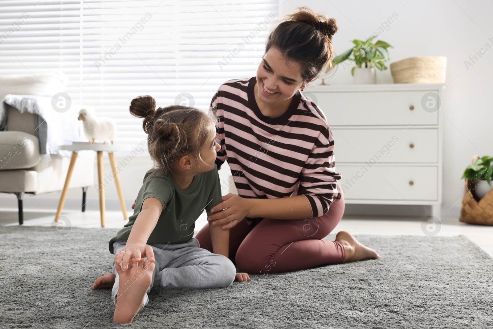 Photo of Young mother and her daughter stretching together at home