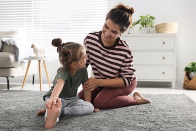 Young mother and her daughter stretching together at home