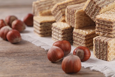 Photo of Delicious wafers with hazelnuts on brown wooden background, closeup