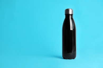 Stylish thermo bottle on light blue background, space for text