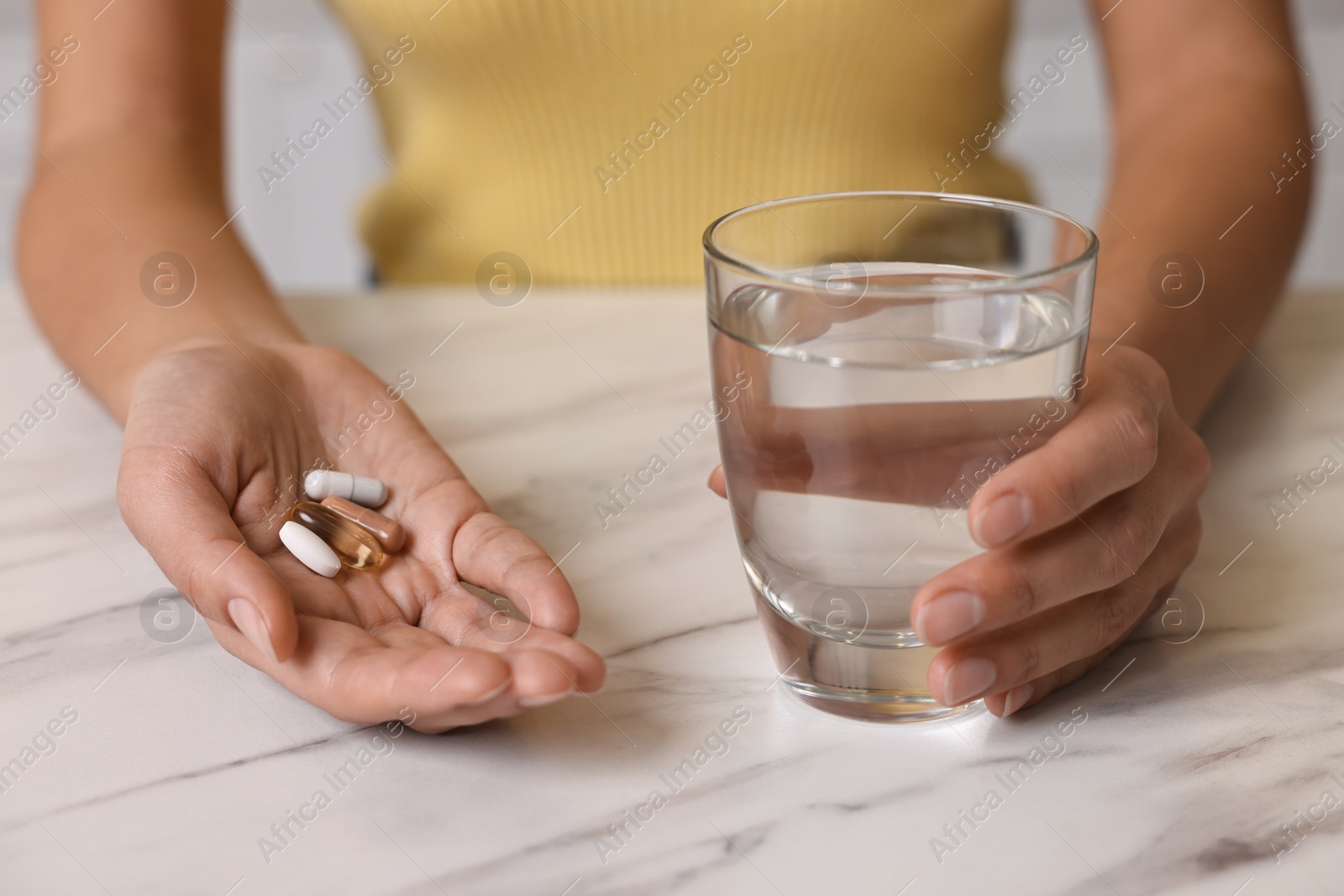 Photo of Woman with vitamin pills and glass of water at white marble table, closeup