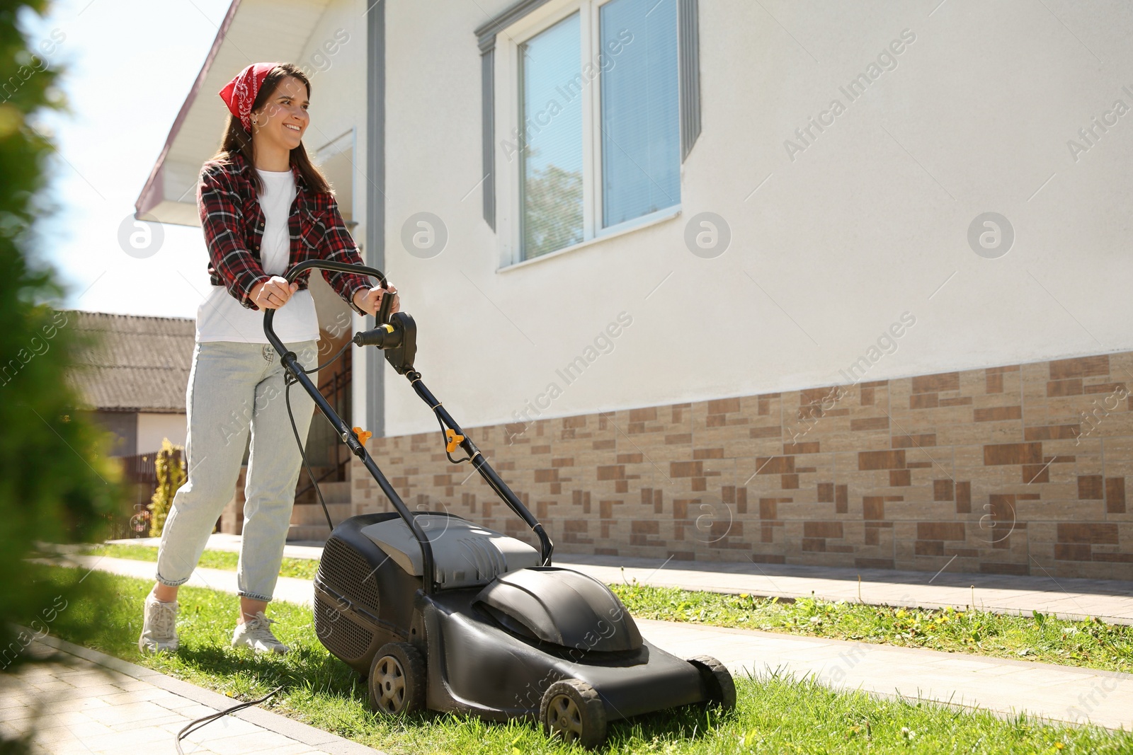 Photo of Woman cutting green grass with lawn mower on backyard