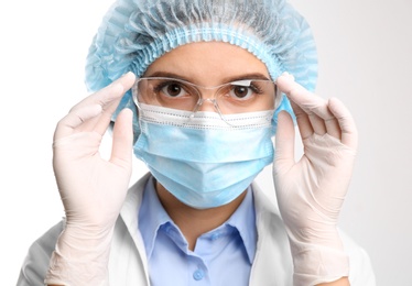 Photo of Doctor with medical gloves, mask, cap and protective goggles on white background, closeup