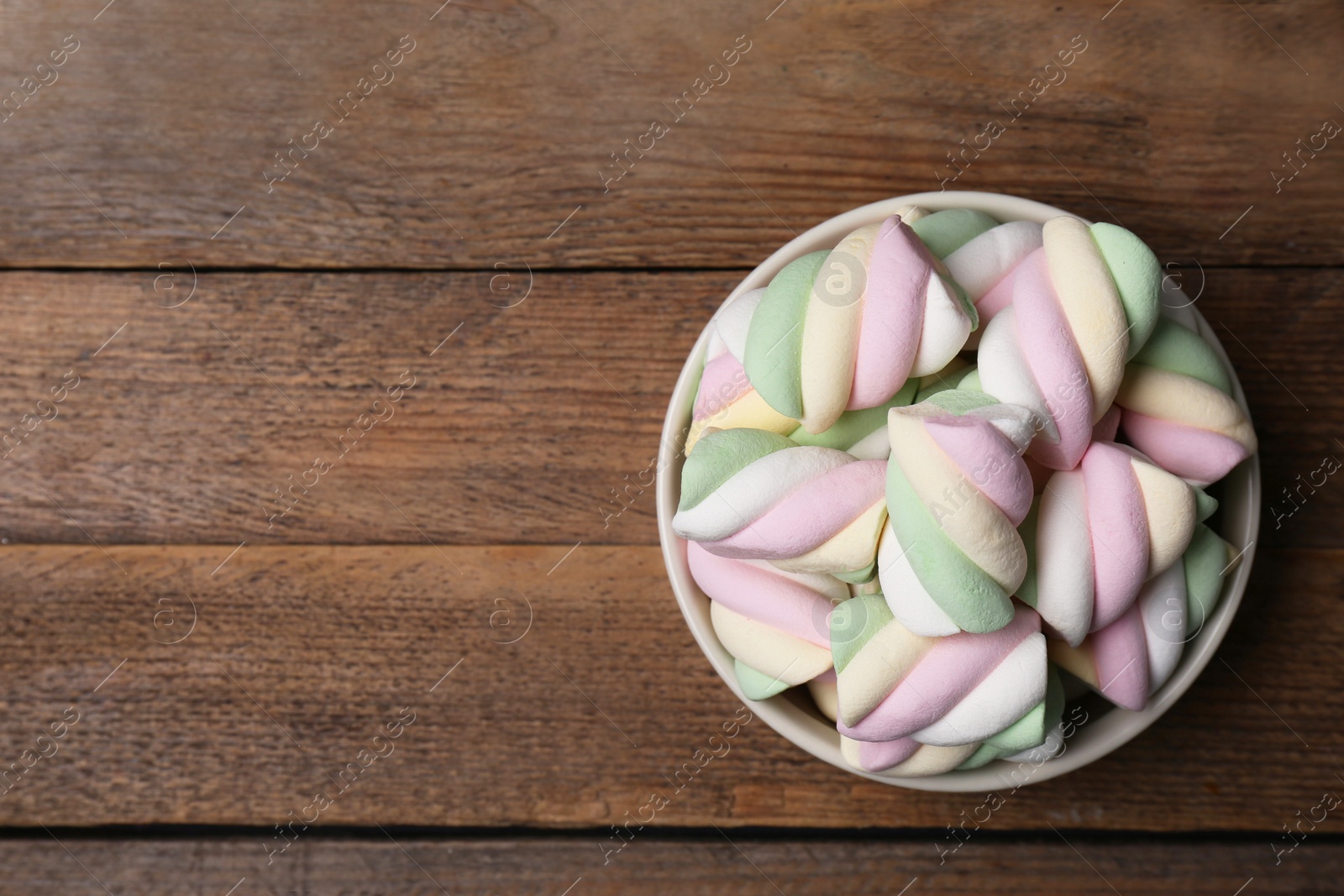 Photo of Bowl with colorful marshmallows on wooden table, top view. Space for text