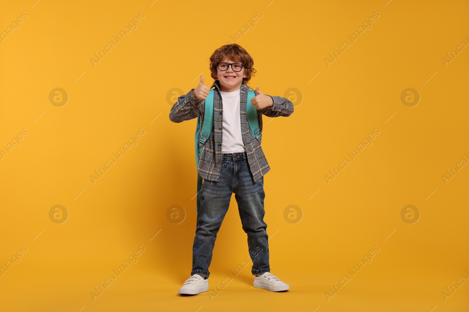 Photo of Happy schoolboy with backpack showing thumbs up gesture on orange background